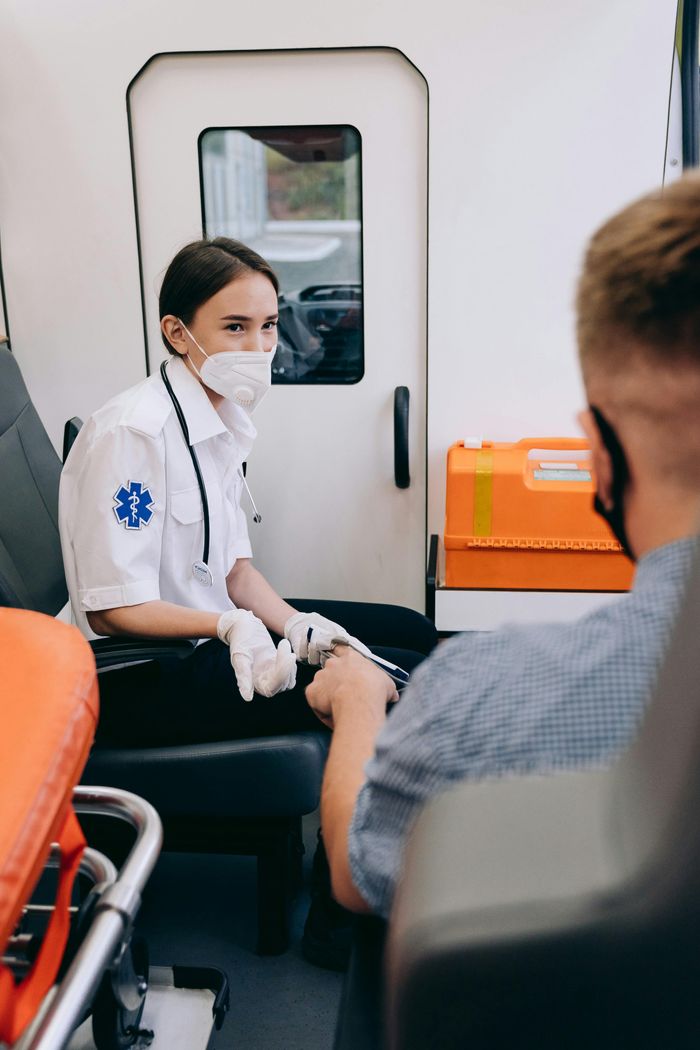A paramedic wearing a mask assists a patient inside an ambulance, ensuring safety and care.